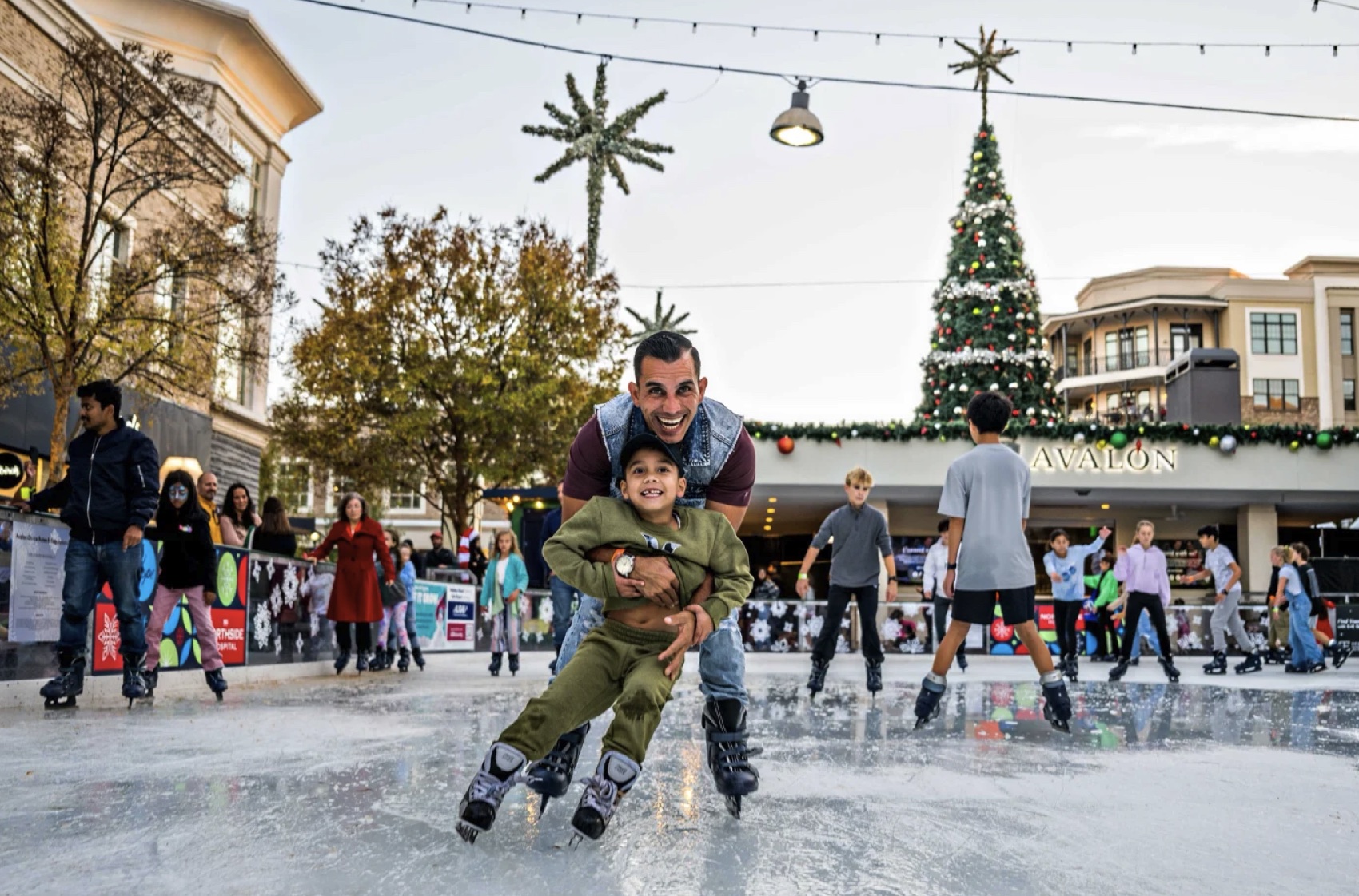 A family skating at the outdoor holiday rink beneath palm trees and a Christmas tree